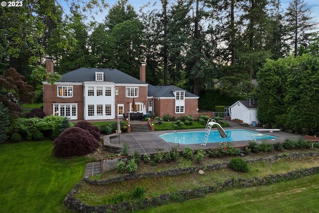 view of swimming pool with an outdoor structure, a water slide, a diving board, a lawn, and a patio area