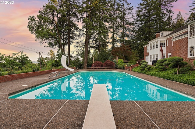 pool at dusk featuring a diving board and a water slide