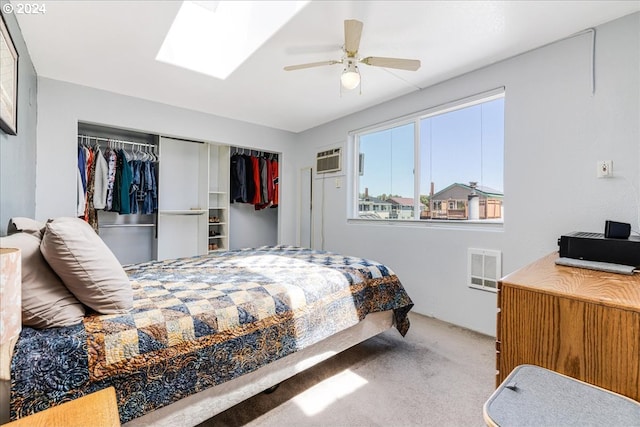 carpeted bedroom with an AC wall unit, a skylight, ceiling fan, and a closet