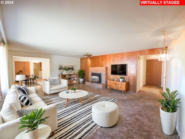 living room featuring wood walls, ceiling fan with notable chandelier, and a tile fireplace