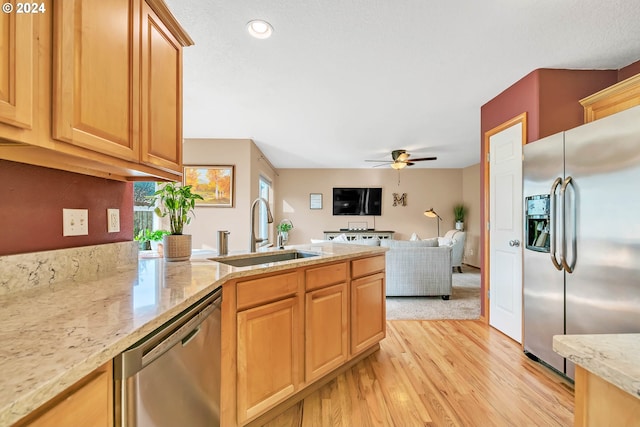 kitchen with light stone countertops, appliances with stainless steel finishes, sink, ceiling fan, and light hardwood / wood-style flooring