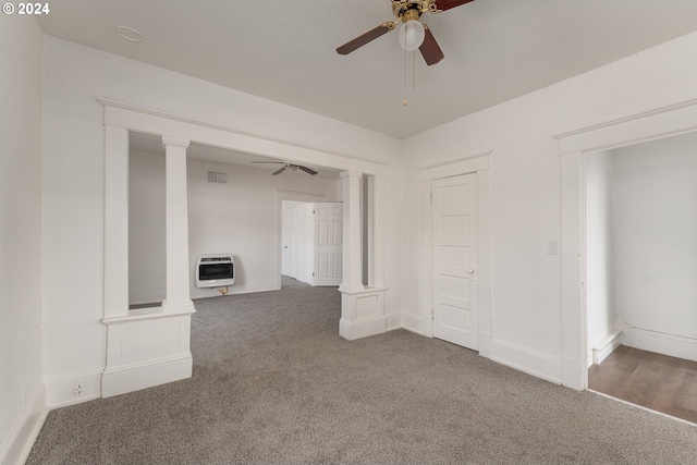 unfurnished living room with dark carpet, ceiling fan, heating unit, and decorative columns