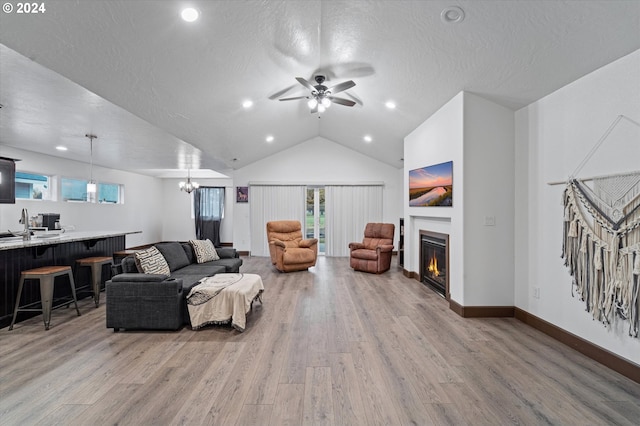 living room with ceiling fan with notable chandelier, light wood-type flooring, lofted ceiling, and sink