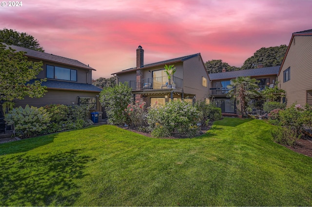 back house at dusk with a lawn and a balcony