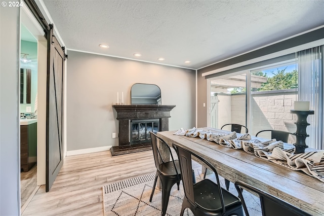 dining area with a barn door, ornamental molding, a textured ceiling, and light wood-type flooring