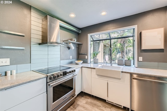 kitchen with light stone countertops, sink, wall chimney exhaust hood, stainless steel appliances, and white cabinets