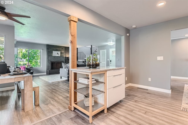 kitchen featuring light hardwood / wood-style flooring, a brick fireplace, ceiling fan, and decorative columns