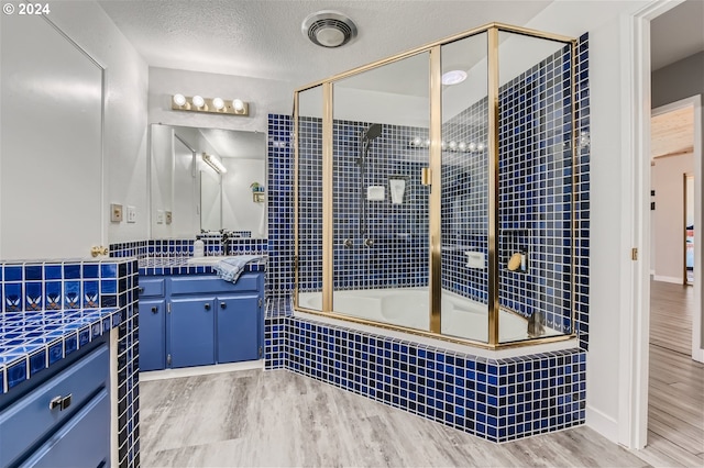 bathroom with hardwood / wood-style flooring, vanity, combined bath / shower with glass door, and a textured ceiling