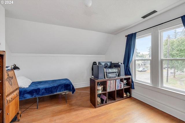 bedroom featuring wood-type flooring, vaulted ceiling, visible vents, and multiple windows