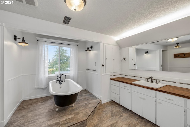 bathroom with backsplash, a textured ceiling, wood-type flooring, a bath, and vanity