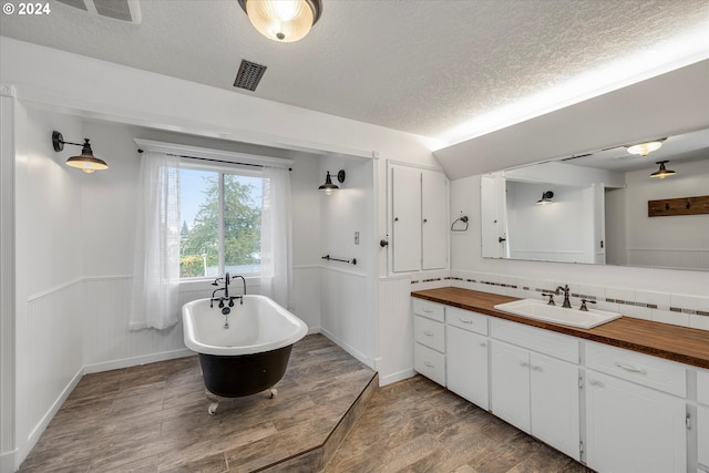 bathroom with a wainscoted wall, a freestanding bath, wood finished floors, vanity, and a textured ceiling