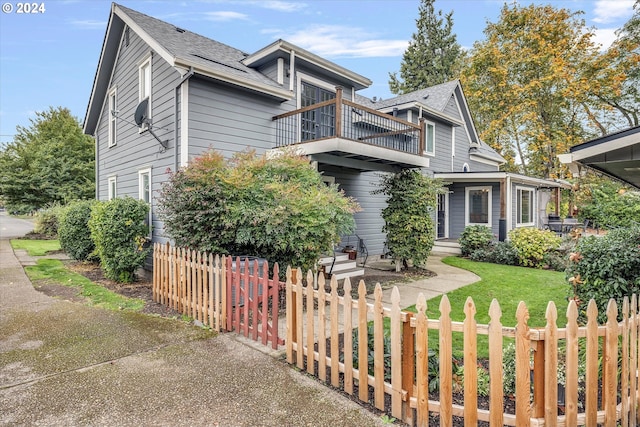 view of front of house featuring a balcony, a front yard, and a fenced front yard