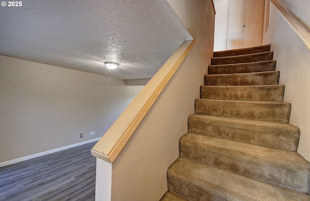 stairway with a textured ceiling, baseboards, and wood finished floors