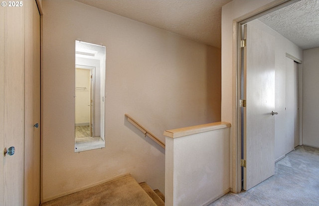 hallway featuring a textured ceiling, carpet flooring, and an upstairs landing