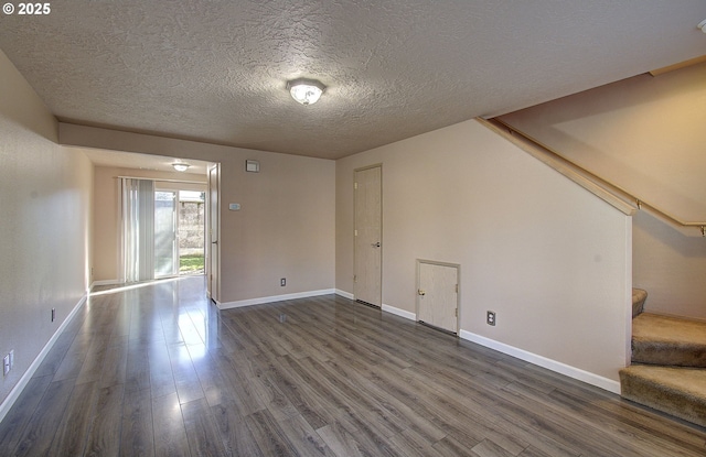 empty room featuring dark wood finished floors, stairway, baseboards, and a textured ceiling