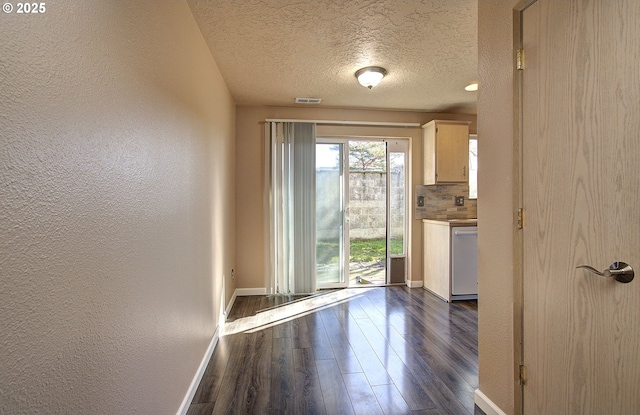 doorway featuring a textured ceiling, a textured wall, dark wood-type flooring, visible vents, and baseboards