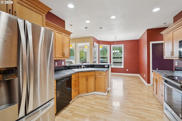 kitchen featuring light hardwood / wood-style floors, stainless steel appliances, decorative light fixtures, dark stone counters, and sink