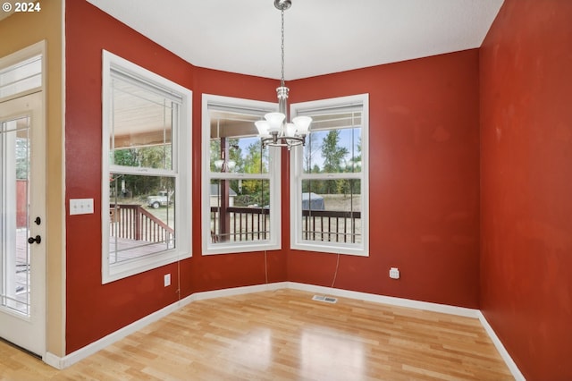 unfurnished dining area featuring wood-type flooring, a chandelier, and a healthy amount of sunlight