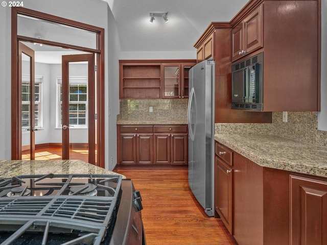 kitchen with stainless steel refrigerator, backsplash, black microwave, light stone countertops, and dark hardwood / wood-style flooring