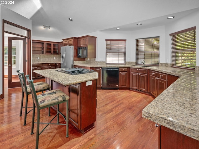 kitchen with sink, a kitchen breakfast bar, a center island, black appliances, and light hardwood / wood-style flooring