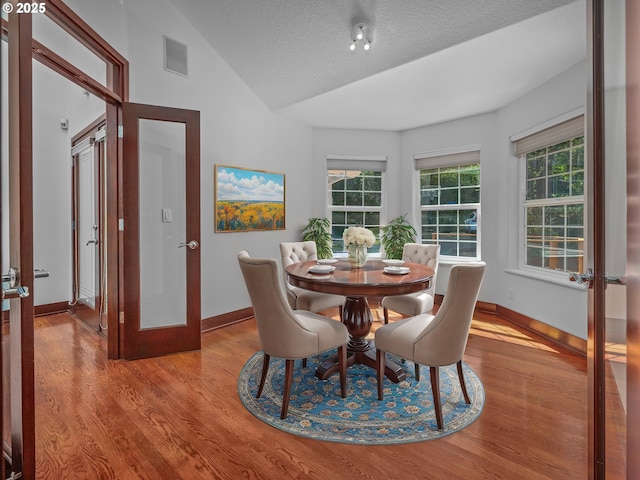 dining space featuring french doors, vaulted ceiling, light hardwood / wood-style floors, and a textured ceiling