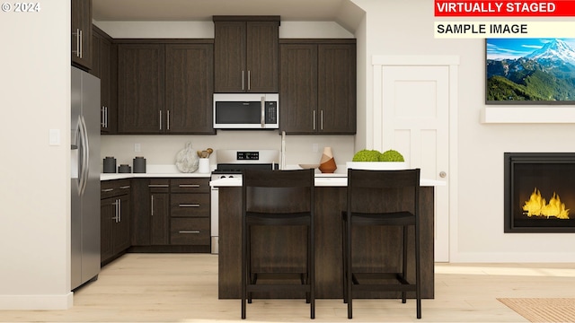 kitchen featuring appliances with stainless steel finishes, dark brown cabinetry, a breakfast bar, and light hardwood / wood-style flooring