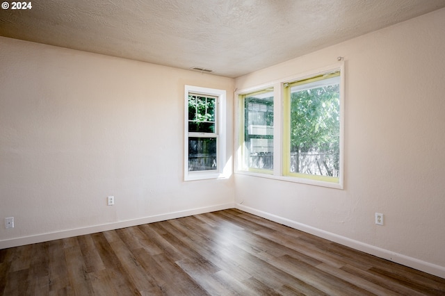 spare room with a textured ceiling, a healthy amount of sunlight, and dark hardwood / wood-style floors