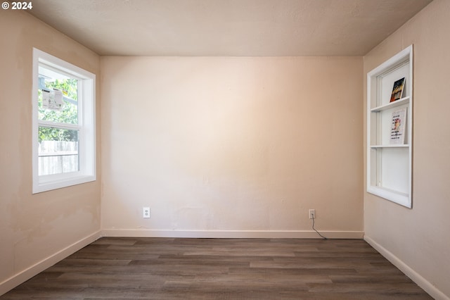 empty room featuring baseboards, dark wood-type flooring, and built in shelves