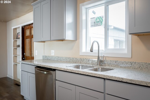 kitchen featuring stainless steel dishwasher, hardwood / wood-style floors, sink, and light stone countertops