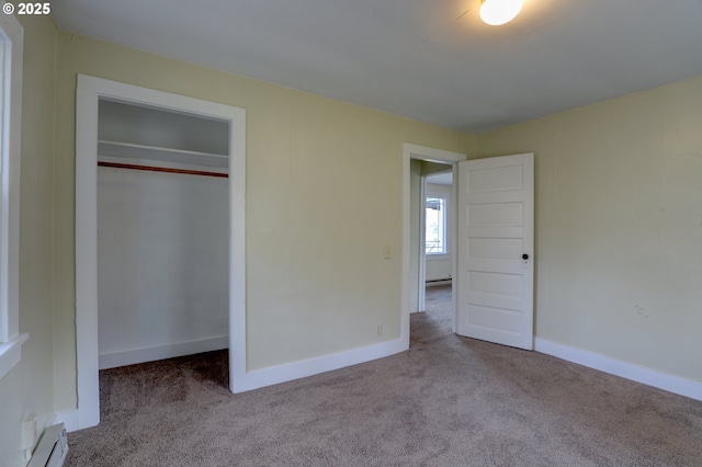 unfurnished bedroom with baseboard heating, a closet, light carpet, and baseboards