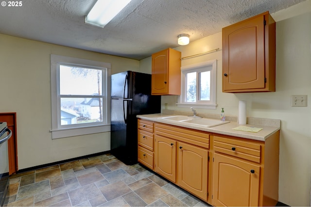 kitchen featuring light countertops, freestanding refrigerator, a sink, a textured ceiling, and baseboards