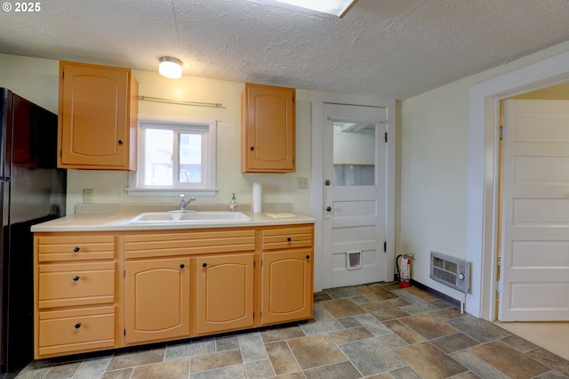 kitchen with freestanding refrigerator, stone finish floor, light countertops, and a sink