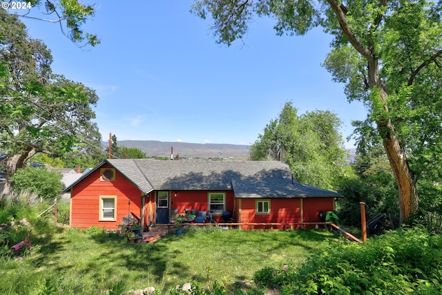 back of property with a yard, a shingled roof, and a mountain view