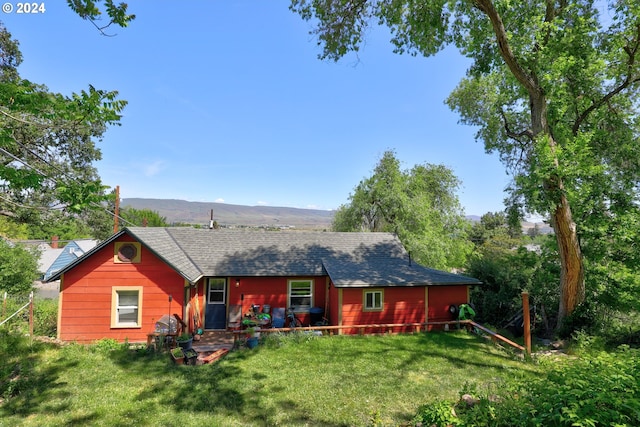 back of property with a shingled roof, a lawn, and a mountain view