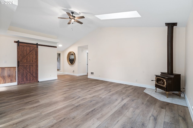 unfurnished living room featuring a wood stove, lofted ceiling with skylight, ceiling fan, and light wood-type flooring