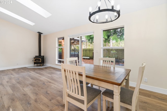 dining space with vaulted ceiling with skylight, light wood-type flooring, a wood stove, and a chandelier