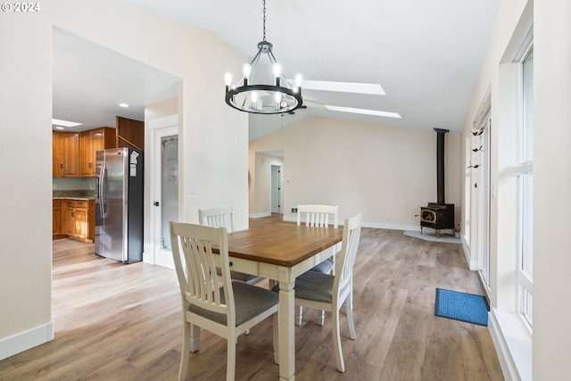 dining area featuring a chandelier, light hardwood / wood-style flooring, a wood stove, and lofted ceiling with skylight