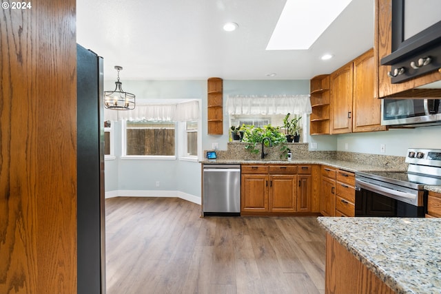 kitchen with light stone countertops, a skylight, stainless steel appliances, sink, and light hardwood / wood-style flooring