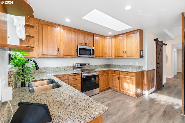 kitchen with a skylight, a barn door, light hardwood / wood-style floors, light stone counters, and stainless steel appliances