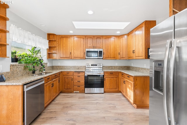 kitchen featuring a skylight, light stone countertops, sink, appliances with stainless steel finishes, and light wood-type flooring