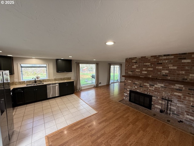 kitchen featuring light wood-type flooring, a wealth of natural light, a fireplace, sink, and dishwasher