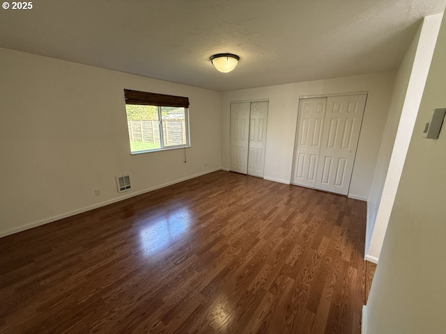 unfurnished bedroom with a textured ceiling, dark wood-type flooring, and two closets