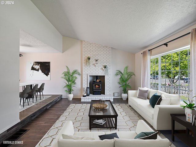 living room with vaulted ceiling, a wood stove, a textured ceiling, and wood-type flooring