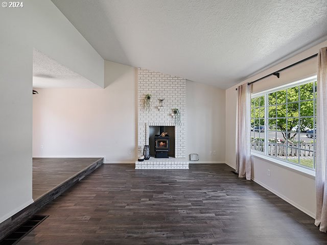 unfurnished living room featuring vaulted ceiling, a textured ceiling, a wood stove, and dark hardwood / wood-style floors