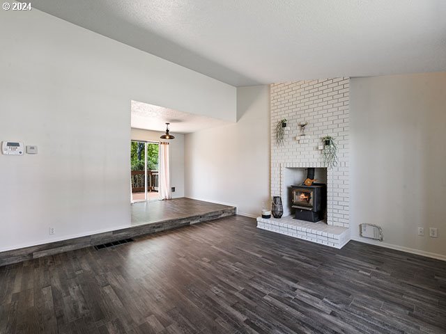 unfurnished living room featuring dark hardwood / wood-style flooring, lofted ceiling, and a wood stove