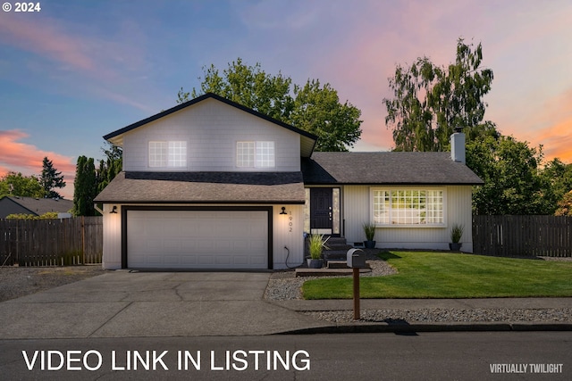 tri-level home with a garage, driveway, fence, and a lawn