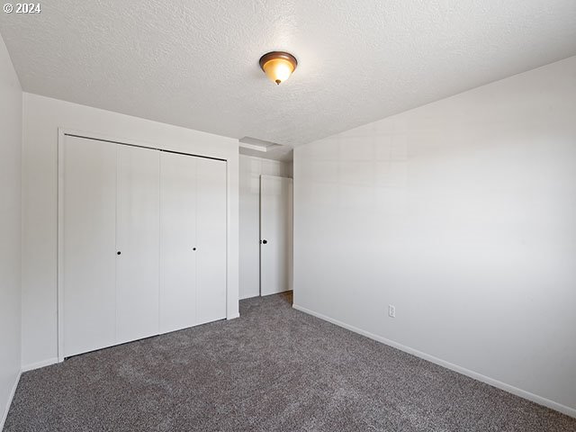 unfurnished bedroom featuring two closets, a textured ceiling, ensuite bath, and dark colored carpet