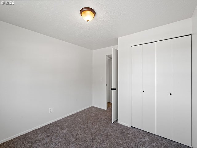 unfurnished bedroom with a textured ceiling, a closet, and dark colored carpet