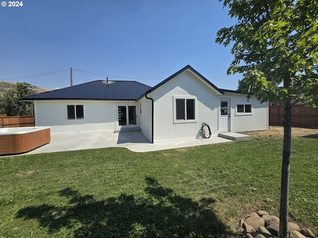 rear view of house with a lawn, a hot tub, and a patio