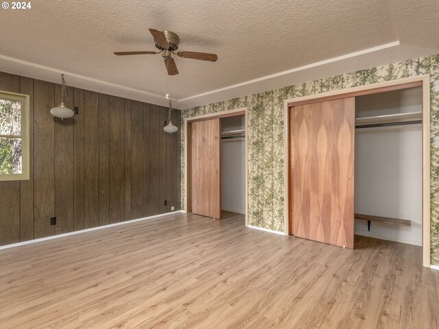 unfurnished room featuring ceiling fan, a textured ceiling, light wood-type flooring, and wood walls